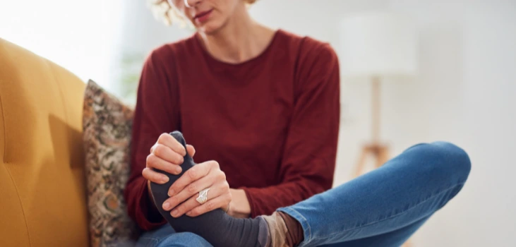 Nooro EMS Foot Massager lady with foot pain touches her foot